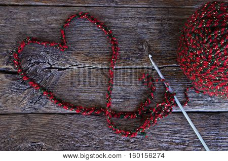 A top view image of a crochet hook and crochet yarn shape in a heart symbol on a wooden table top.