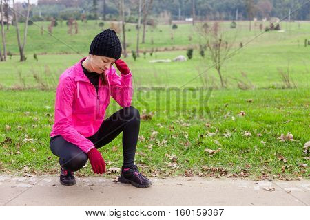 Young woman athlete feeling lightheaded or with headache on a cold winter day in the track of an urban park.
