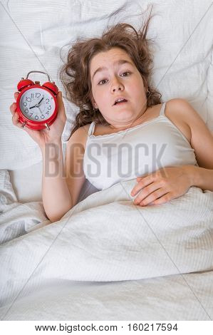 Young woman is waking up. She oversleep and is shocked.