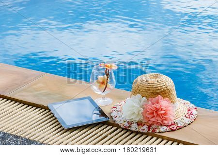 Hat woman and tablet beside swimming pool on weekend vacation concept