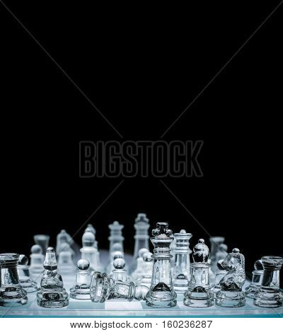 Close-up view of transparent glass chess board with chess pieces on black background