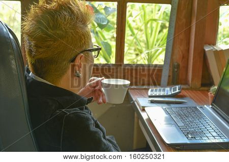 Woman drinking coffee at office desk in the morning.