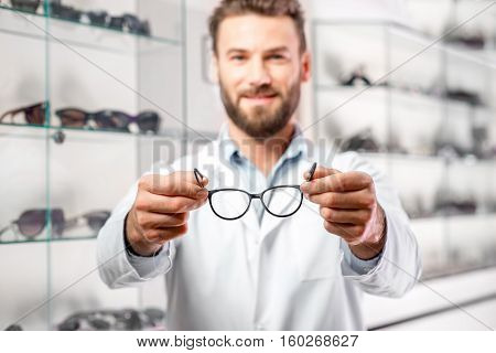 Handsome ophthalmologist holding eyeglasses for a try out. Optometrist offering to wear a pair of glasses. Image with small deph of field focused on the hands and glasses
