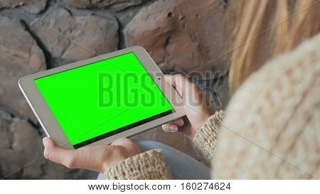 Woman looking at horizontal tablet computer with green screen. Close up shot of woman's hands with pad