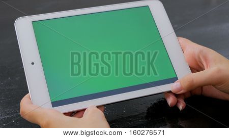 Woman looking at horizontal tablet computer with green screen. Close up shot of woman's hands with pad