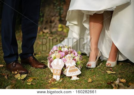 Close-up photo of bride and groom footwear with a wedding bouquet and gingerbread in a shape of traditional slovak old style wedding couple. Photo is taken during autumn sunny day in a garden.