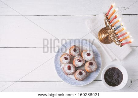 Hanukkah menorah and sufganiot on the white wooden table top view