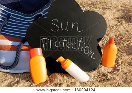 Black board with inscription, beach bag and sunscreen cream on sea coast