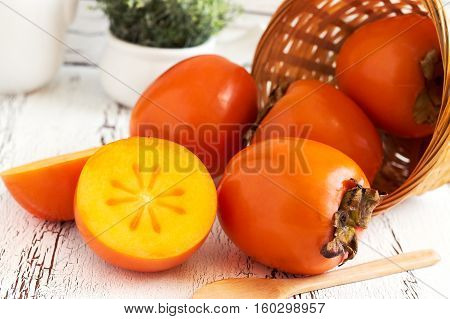 Japanese persimmon (Diospyros kaki) in woven basket on white rustic wooden background