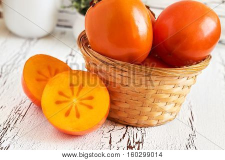 Japanese persimmon (Diospyros kaki) in woven basket on white rustic wooden background