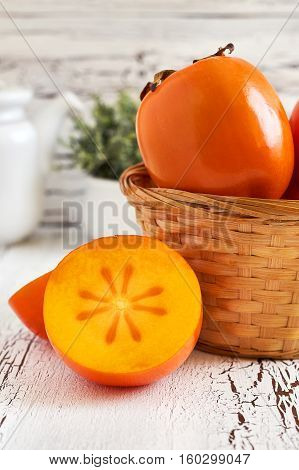 Japanese persimmon (Diospyros kaki) in woven basket on white rustic wooden background. Copy space