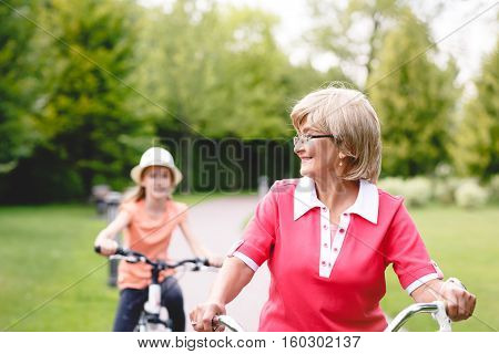 Happy active senior woman riding bike with her grandaughter in park at summer
