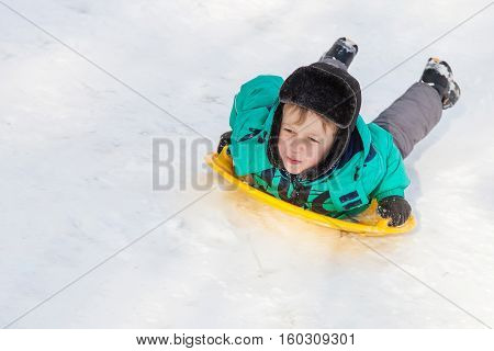 Boy sliding down the hill on saucer sleds outdoors winter day ride down the hills winter games and fun