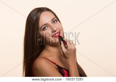 Young model woman smiling while doing makeup isolated on white. Pretty lady painting lips with red lipstick and looking at camera.