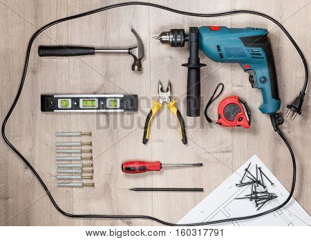 Set of construction tools to repair on a wooden surface: drill, hammer, pliers, self-tapping screws, roulette, construction level, drawing, construction pencil. Top view