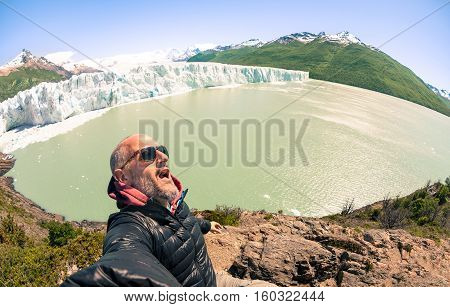 Young man solo traveler taking selfie at Perito Moreno glaciar in south american argentinian Patagonia - Adventure wanderlust concept on world famous nature wonder in Argentina - Warm turquoise filter