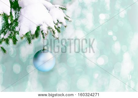Snow covered fir branch with pale blue Christmas ornament. Christmas greeting background with fir branch and blue ball. Christmas decoration with bauble hanging. Copy space.