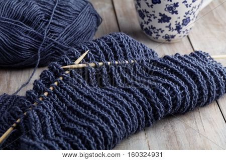 Knitting needles with unfinished scarf on a rustic table