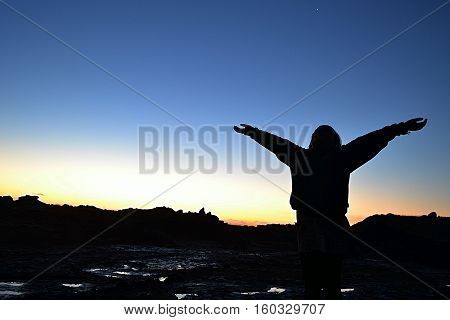 silhouette of child reaching up to the sky at sunset