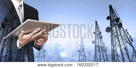 Businessman working digital tablet, with double exposure panoramic cityscape and telecommunication towers in sunrise