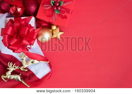Christmas background decorations gift boxes inside santa claus hat with two gold reindeer and red ribbon bow with ornament bauble on red backdrop with copy space still life style Greeting card for new year
