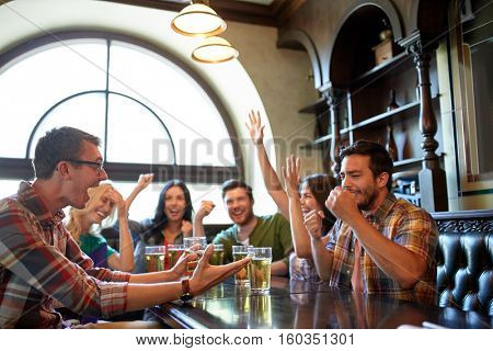 people, leisure, friendship and entertainment concept - happy friends drinking beer, watching sport game or football match and celebrating victory at bar or pub