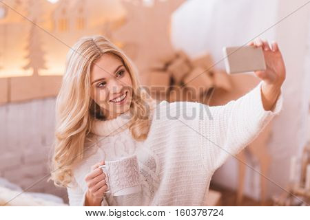 Time for a selfie. Happy attractive young woman holding a smartphone and looking at its camera while taking a selfie