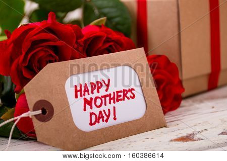 Roses near Mother's Day tag. Flowers and present on wood. Ingenuity in making presents.
