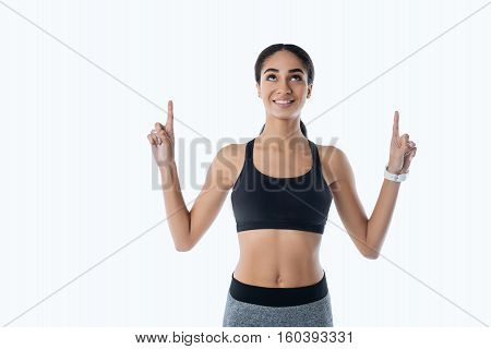 Do not give up. Healthy sporty girl holding arms bent in elbow pointing upwards, standing over white background
