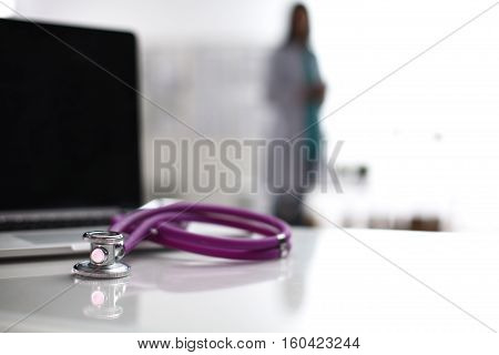 Laptop and stethoscope on the desk doctors standing in the background.