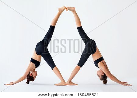 Two young women doing partner yoga asana downward facing dog. Adho Mukha Svanasana