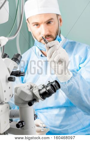 Eye surgeon holding small surgical scissors for eye operation in the operating room near the microscope. Image with small deph of field focused on hands and scissors