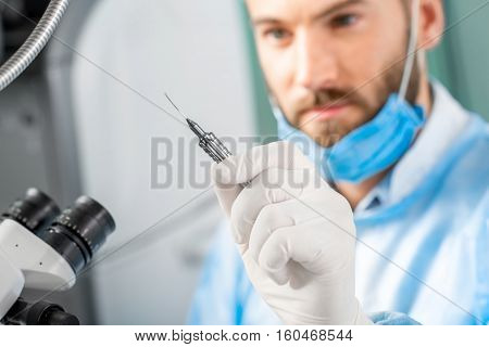 Eye surgeon holding small surgical scissors for eye operation in the operating room near the microscope. Image with small deph of field focused on hands and scissors