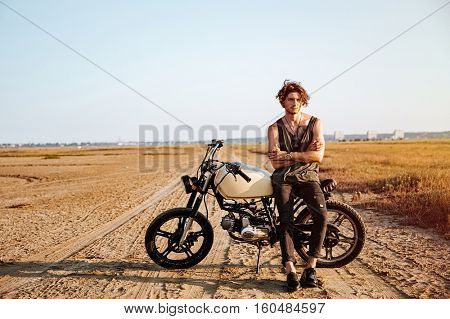 Young brutal man in black leaning on a motorcycle