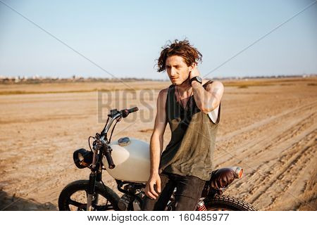 Young brutal man in black leaning on a motorcycle
