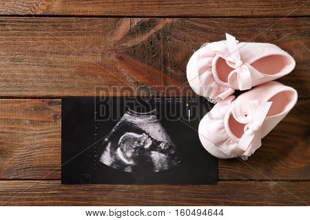 Ultrasound picture of baby and children shoes on wooden background
