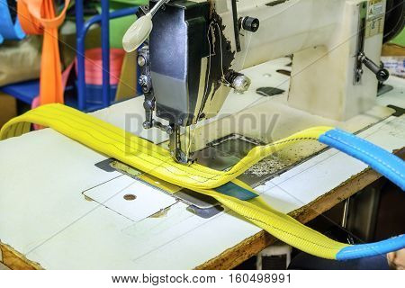 Industrial sewing machine sews a webbing sling. Manufacture of textile slings and tie straps.
