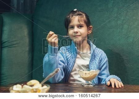 young girl eats ice cream with a spoon at the table in cafe