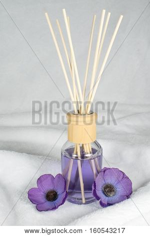 A decorative bottle with purple fragrance oil along with beautiful poppy flowers on a fluffy underground