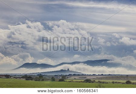Early afternoon scenery of cereals fields and little town with castle between the fog Nogales Spain