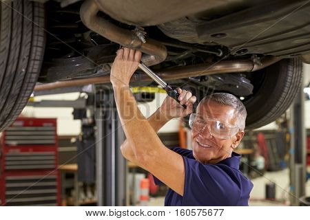 Portrait Of Auto Mechanic Working Underneath Car In Garage
