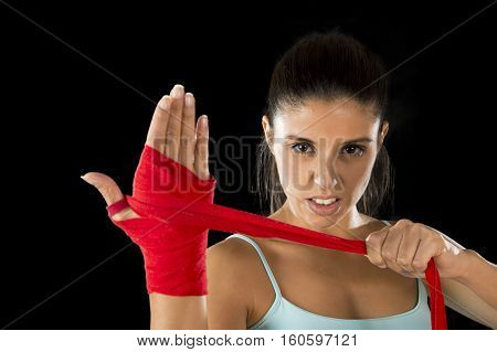 young attractive hispanic fitness woman doing self hand wraps before boxing or fighting workout isolated on black background looking fierce concentrated and confident