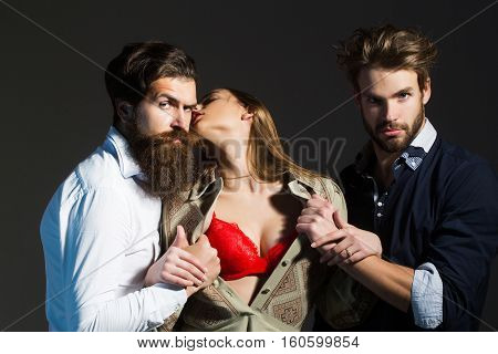 Young people or friends of two bearded handsome men hipsters with beards and pretty cute girl or sexi beautiful woman in red bra on grey wall
