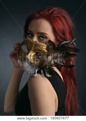 Beautiful redheaded woman in black dress with carnival mask