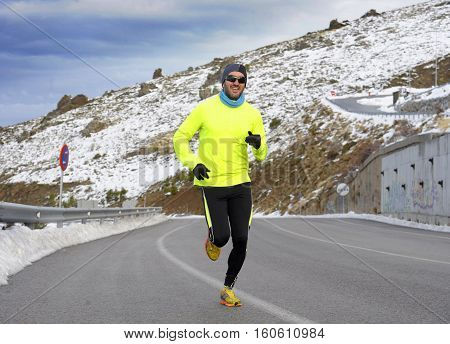young healthy sport man running on asphalt road at snow mountains in trail runner hard workout in energy and endurance concept with a beautiful cold winter background