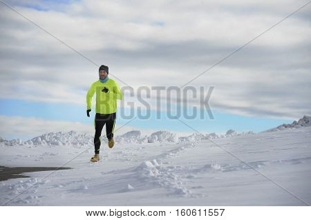 young healthy sport man running in snow mountains in trail runner hard workout in energy and endurance concept with a beautiful cold winter background