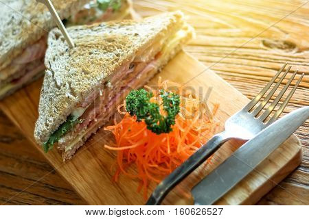 Club sandwich on the wood plate decorate with chopped carrot and parsley together with fork and knight on the bark wood table background