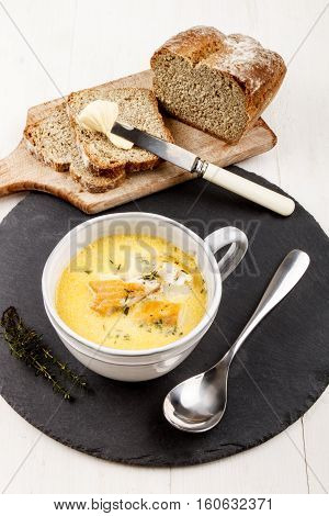 traditional scottish fish soup cullen skink with potatoes in a gray clay cup on a round slate and home baked soda bread on wooden board