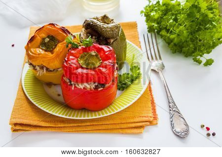 Baked bell peppers yellow red and green ones stuffed with minced meat and rice. Fresh parsley white table.