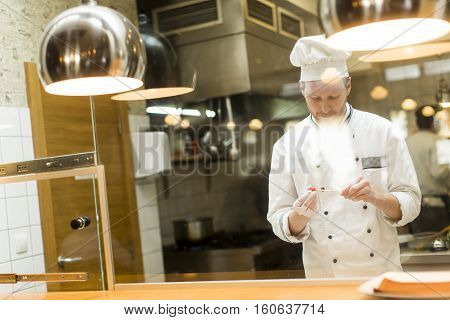 Young chef with white uniform standing at a modern kitchen in the restaurant and preparing food
